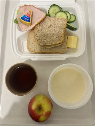 Zdjęcie przedstawia pojemnik jednorazowy biodegradowalny a w nim zupa mleczna,chleb pszenny i chleb graham,masło,og&oacute;rek, wędlina,serek topiony,sałata,herbata czarna,jabłko.