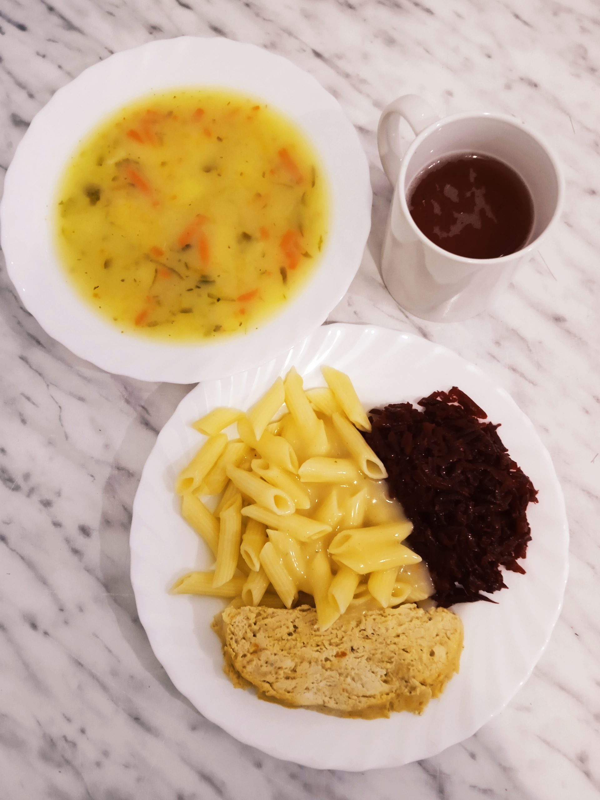 na zdjęciu obiad złożony z dwóch dań. Na talerzu głębokim zupa ogórkowa, na talerzu płaskim makaron z sosem mięsnym, mięso i buraczki. Powyżej talerzy kubek z kompotem