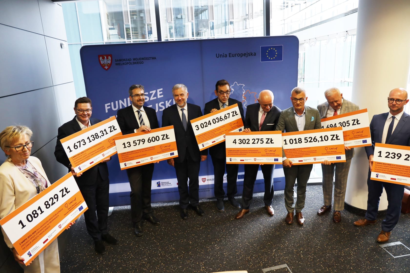 zdjęcie przedstawia dziewięciu delegatów szpitali, które otrzymały dofinansowanie w ramach programu Regionalnego. Każdy trzyma w rękach plansze z przyznana kwota dofinansowania.